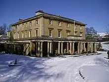 a country house with a portico along the front of it, there is snow on the ground