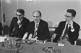 Andreas Papandrou flanked by two men seated at a table in front of microphones
