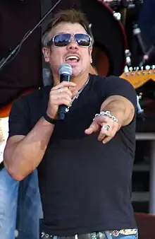 A man wearing dark glasses and a dark T-shirt singing into a microphone