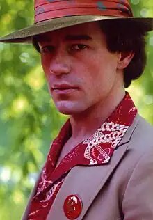 A colored, self-portrait photograph of a man wearing a hat and a suit.