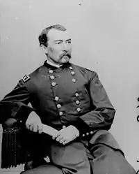 Man with moustache sitting down with arm on table in uniform with two columns of buttons