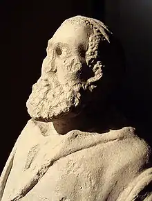 Head and upper body of a statue depicting an old man with a large beard. Minimal damage includes a missing nose.