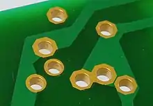 Close-up view of an electronic circuit board showing component lead holes (gold-plated) with through-hole plating.