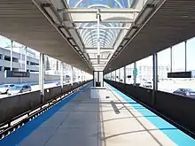 A train platform with tracks on either side. A digital sign hangs from an overhead canopy.