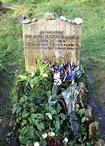 Flowers in front of a simple headstone bearing the inscription, "In memory Sylvia Plath Hughes 1932–1963 Even amidst fierce flames the golden lotus can be planted."