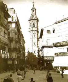 a plaza between several buildings with a bell tower in the center phot is yellowed with age