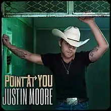 A man wearing a black t-shirt, blue jeans and white cowboy hat, inside a freight elevator while holding the cage cover.