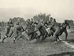 A cluster of American football players colliding on a dirt field