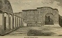 An old black and white image of the ruins of a grassy courtyard surrounded by columns and buildings