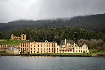 Photo of the main penitentiary building, partially ruined and hollowed out, with thickly forested hills in background