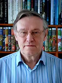 head and shoulder colour photograph of a white man in glasses and a blue shirt in front of a bookcase