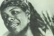 Black-and-white photograph of a African American woman in her forties, wearing a bandana and raising her left hand.