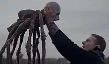 A man reaching out and touching a spider-like creature with a human face