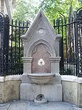 A Gothic drinking fountain and metal railings, with a park visible at an elevated level through the railings. An inscription on the drinking fountain reads "James & Mary Ann Ward late of Aldersgate and Islington Erected by their daughters 1876".