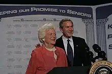 Barbara Bush and George W. Bush stand in front of a backdrop reading "Keeping Our Promise to Seniors"