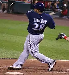 A man in a navy baseball jersey and batting helmet with gray pants