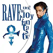 Prince wearing a blue, skin-tight outfit stands in front of a white background, staring into the camera.