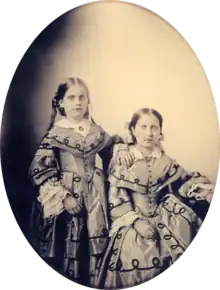 An oval, framed photographic portrait of two young girls dressed in elaborate Victorian-era gowns
