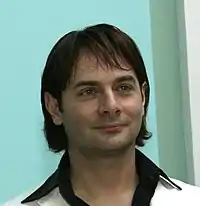 Head of man in his thirties with tousled hair sticking up and a small mustache