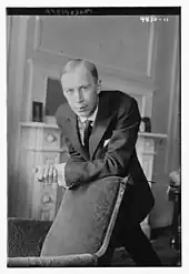 A black-and-white photograph of a man leaning on a chair