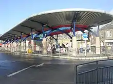 An open-air bus station with a canopy, in front of stone buildings