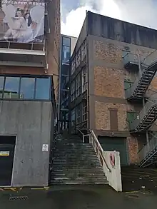 two buildings, one old (brick), one new with concrete stairs leading up between them