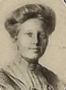 A white woman with fair hair dressed in bouffant updo, wearing a high-collared blouse
