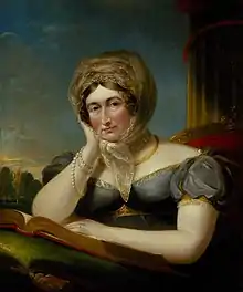 Caroline is seated, resting her hand on a book