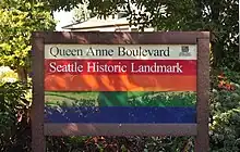 photograph of a sign created by the Parks and Recreation department for Queen Anne Boulevard.  It has horizontal stripes in cream, red, orange, green, and blue (from top to bottom)