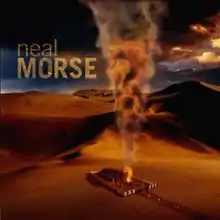 A small ranch house, surrounded by a white fence, in the middle of a vast desert with a fire emanating from its front yard space.