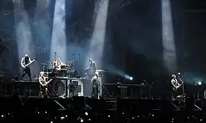 Rammstein performing in August 2013; upper level (left to right): Oliver Riedel, Christoph Schneider, and Christian Lorenz; lower level (left to right): Paul Landers, Till Lindemann, and Richard Kruspe