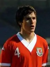 A footballer with dark hair wearing a red jersey