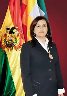 Official portrait of Rebeca Delgado flanked to the left by the Bolivian tricolor and the Wiphala.