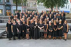 2016 photograph of a choir on stairs outside the Bruges Cathedral, with the Old Town in the background