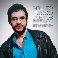 Square with several shades of gray and a picture of Renato Russo facing the camera. 'Renato Russo Duetos' and a list of special guests are written to his right.
