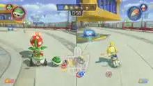 Two characters in split-screen view on a concrete surface. On the left is Bowser Jr., a yellow turtle-like creature with a spiked green shell who is riding in a small circular car. In front of him is a Piranha Plant, a venus flytrap-like creature with a white-spotted red head. On the right is Isabelle, a humanoid yellow dog on a motorbike. Isabelle is driving towards a blue switch with a key icon placed below a yellow and blue cage. In the center of the screen is a minimap displaying the characters' location in the course.