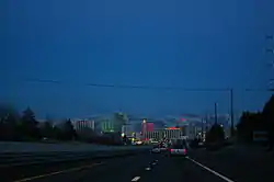 Dusk view of a freeway descending into a neon lit cityscape.