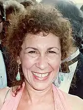 Smiling young woman with short, curly brown hair and sunglasses