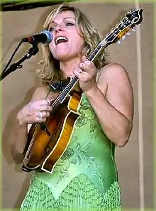 A blonde woman in a green dress singing and playing the mandolin.