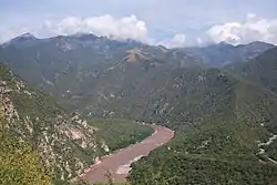 A muddy river winds along the bottom of a deep canyon.