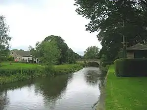 A river running between green lawns and a bridge in the distance