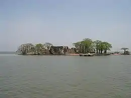 A distant view of very small island home to several thin trees, a brown dock, and a partially obstructed brown shack.