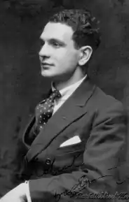 Youngish white man, clean-shaven, with full head of dark hair, seated in left profile, wearing lounge suit and collar and tie