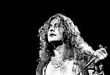 A black and white photograph showing a headshot of Robert Plant with a microphone in hand