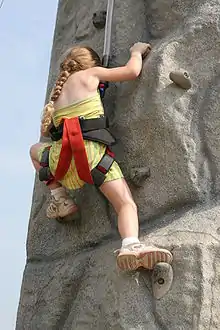 Climbing a rock-textured wall with belay, modular hand holds, incuts, and protrusions