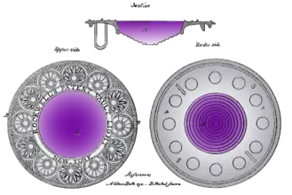 A large circular glass lens with a flat top and a stepped domed bottom. The glass is purple, with the shade darkening towards the top. The glass is set in a wide and ornate circular frame engraved with a semi-geometric ring-of-roundels design that looks a bit Art Deco, although from 1834.