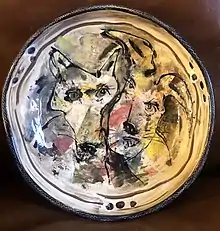 A large ceramic bowl with painted heads of a fox and a hare against a colorful clay background. The artist's fingermarks are visible in black in numerous spots around the rim of the bowl.
