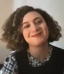 smiling headshot of a women with head tilted and very curly brown hair