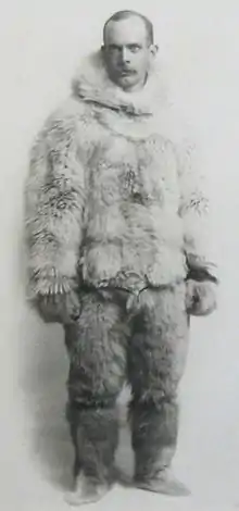 A black-and-white photo of a man wearing animal-skin clothing for cold-weather travel
