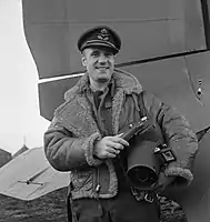 Flight Lieutenant L H Abbott, British Air Ministry official photographer, pictured holding a Fairchild K-20 hand-held aerial camera in front of a Douglas Dakota, World War II